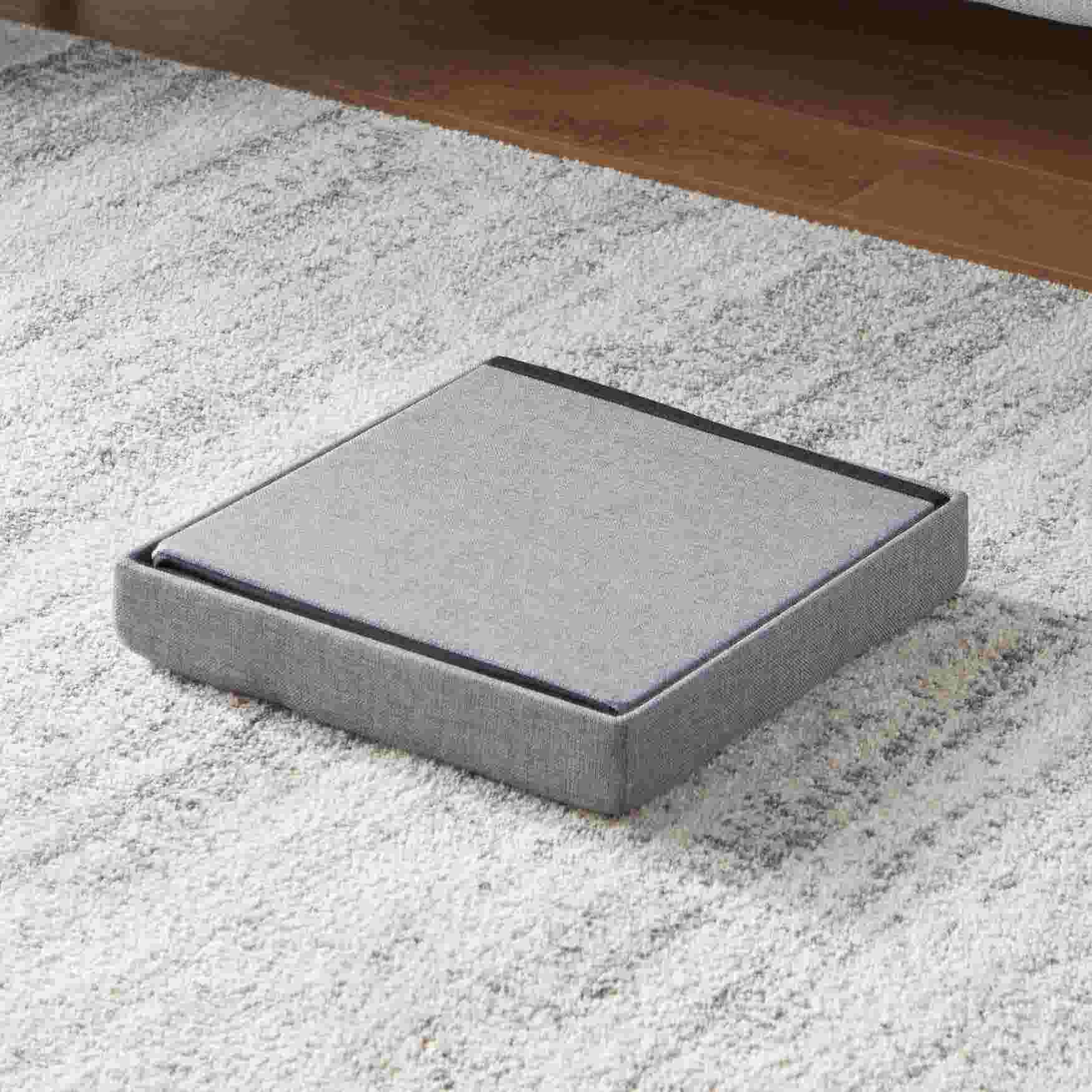 Gray foldable ottoman with a flat top, shown on a rug.
